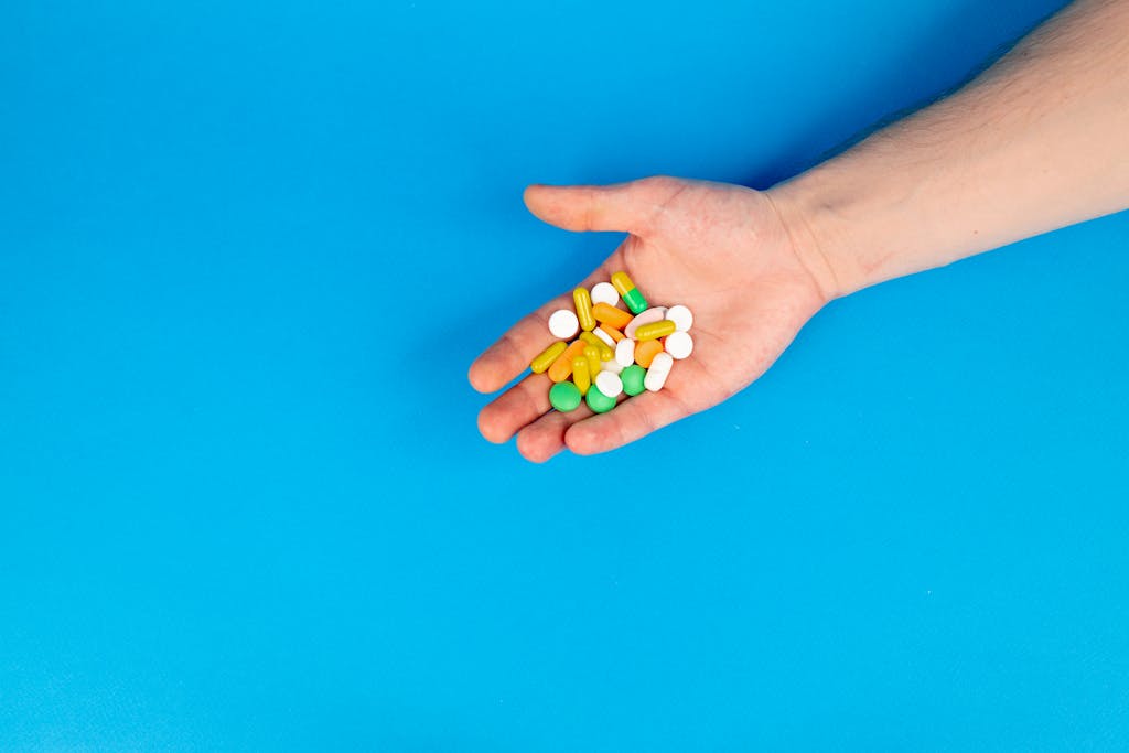A hand holding a variety of colorful pills against a blue background with ample copy space.