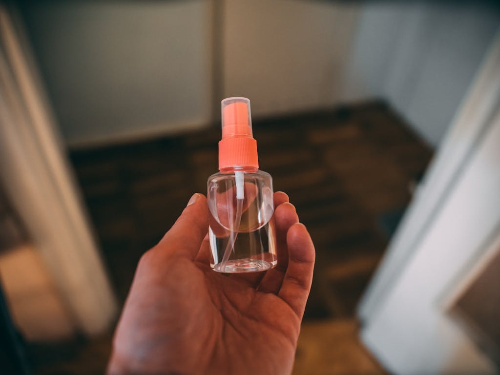 Close-up of a hand holding a clear plastic spray bottle indoors, suitable for healthcare use.