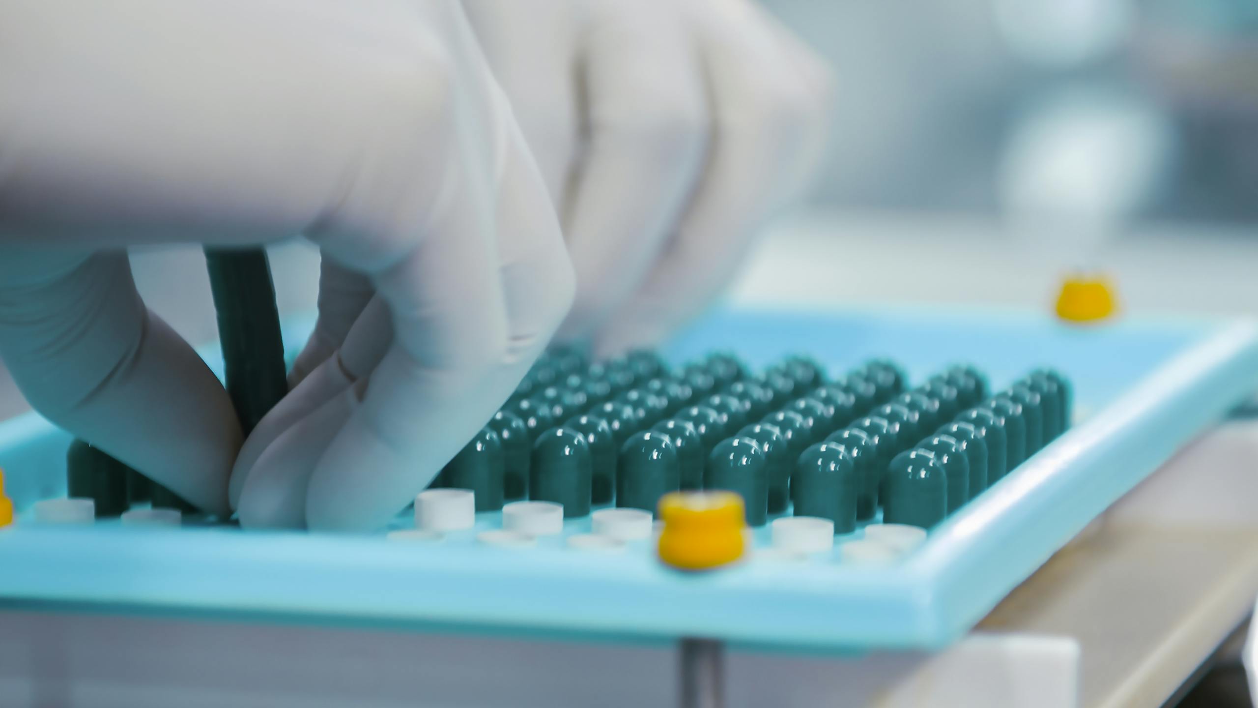 Close-up of gloved hands working with capsules in a pharmaceutical lab setting.